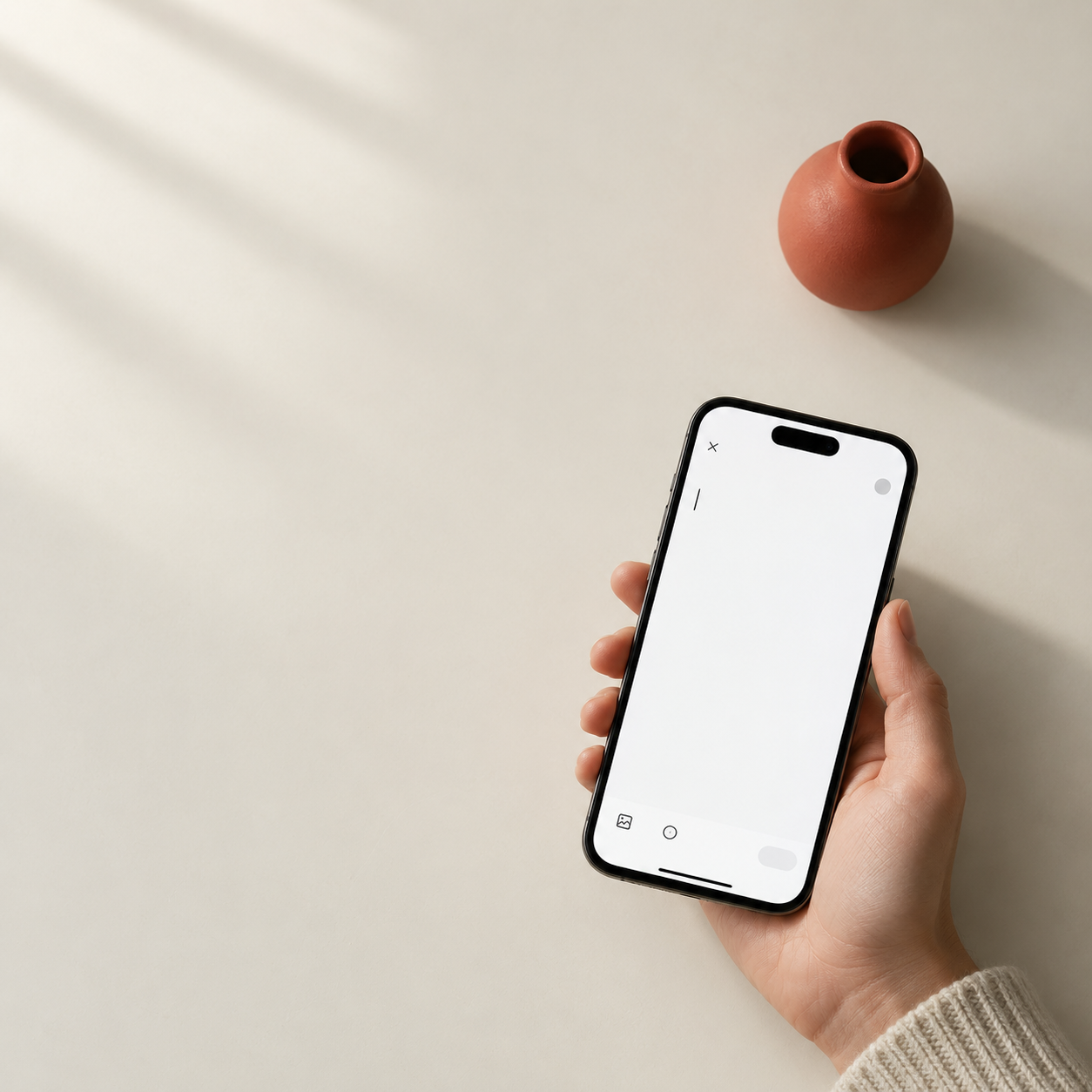 A phone held in warm natural light, beside a terracotta vase